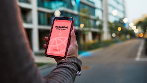 Eine Frau hält ein Mobiltelefon auf der eine Buchungsbestätigung zu sehen ist © przemekklos_photocase Foto: przemekklos