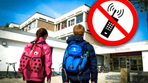 Eine junge Schülerin und ein junger Schüler gehen Richtung eines Schulgebäudes, daneben ist ein Symbolbild mit einem roten Schild zu erkennen, auf dem ein durchgestrichenes Handy abgebildet ist © picture alliance / M.i.S. | M.i.S.-Sportfoto 