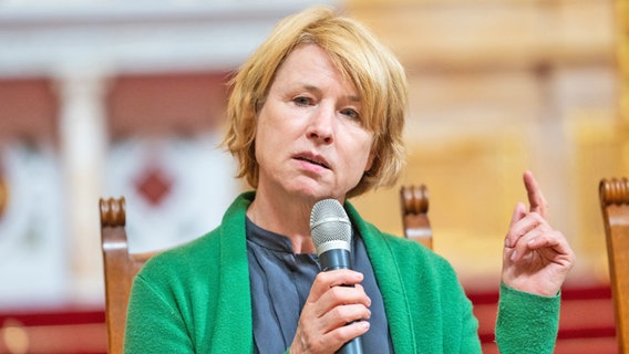 Eine Frau mit hellen Haaren und grünem Oberteil hält eine Hand erhoben, die andere hält ein Mikrofon (Corinna Harfouch) © picture alliance/dpa | Christophe Gateau Foto: Christophe Gateau