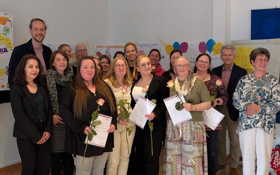 Eine Gruppe erwachsener Menschen mit Blumen und Zertifikaten.
