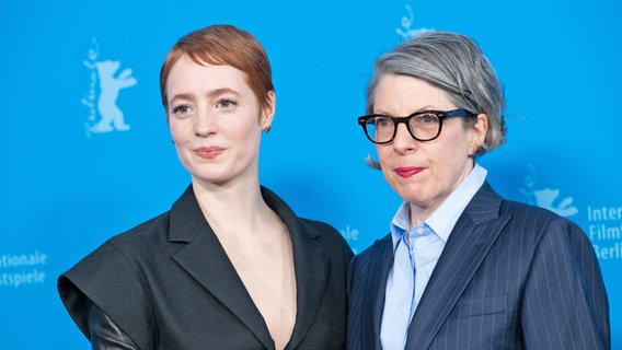 eine junge Frau mit kurzen Haaren und schwarzem Kleid steht neben eine etwas älteren mit Bubi-Schopf und Brille mit blauem Hemd und Sakko © Berlinale 2025 / Ali Ghandtschi Foto: Ali Ghandtschi