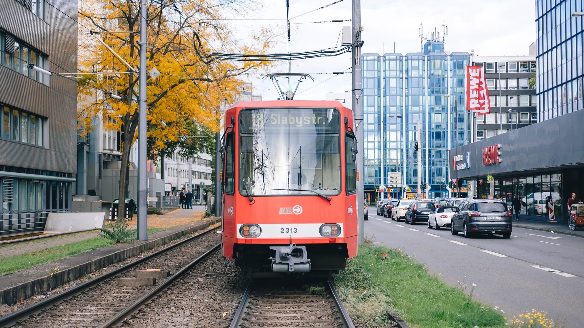 In Cologne, streetcar line 18 towards Slabystrasse is parked in front of Barbarossaplatz, waiting.