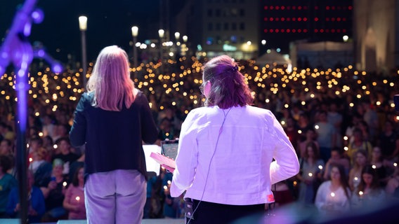 Eine Band steht mit dem Rücken zur Kamera auf einer Bühne, das Publikum hält Kerzen in den Händen. © Kirchentag Foto: Hartmann