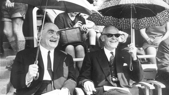 Ein Schwarz-Weiß-Foto mit zwei lachenden Männern, die aufgespannte Regenschirme halten. (Bischof Kurt Scharf (l) und Willem Visser't Hooft, ehemaliger Generalsekretär des Weltkirchenrates) © picture-alliance / dpa Foto: Wolfgang Weihs