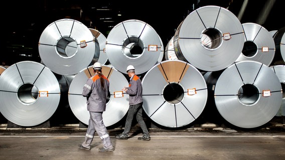 Zwei Mitarbeiter gehen vor aufgewickelten Metallbändern, sogenannten Coils, in einer Halle auf dem Gelände der Salzgitter AG entlang. © picture alliance/dpa Foto: Hauke-Christian Dittrich