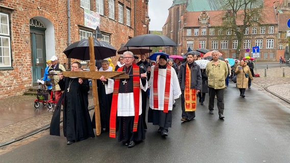 Ein Bischof und eine Pfarerin tragen ein Kreuz in einer Prozession auf einer Straße in Lübeck beim ökumenischen Kreuzweg am Karfreitag. © NDR Foto: Linda Ebener