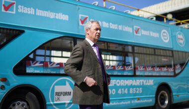 Nigel Farage steht während seiner Wahlkampftour vor einem hellblauen Werbebus seiner Partei Reform UK.