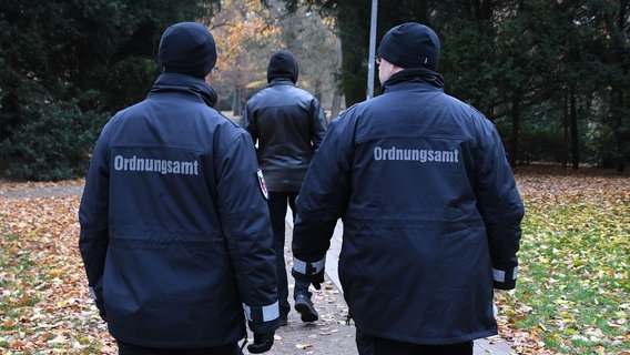 Zwei Beamte des Ordnungsamtes laufen durch einen Park einem Mann hinterher. © picture alliance Foto: Carmen Jaspersen