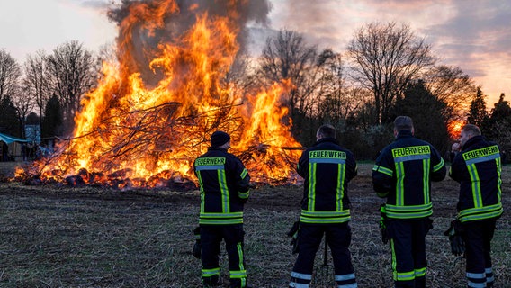 Vor einem Osterfeuer stehen vier Feuerwehrmänner. © picture alliance / Fotostand Foto: Fotostand / Reiss