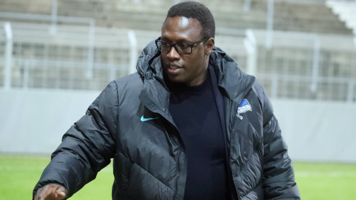 © imago - Das Bild zeigt den Ex-Fußballer Pablo Thiam in seiner Funktion als Nachwuchschef von Hertha BSC. Er trägt eine dunkle Steppjacke mit dem Hertha-Logo auf der linken Seite. Thiam steht im Freien, vermutlich in einem Stadion oder auf einem Sportplatz. Im Hintergrund sind Tribünen und ein Zaun zu sehen. 