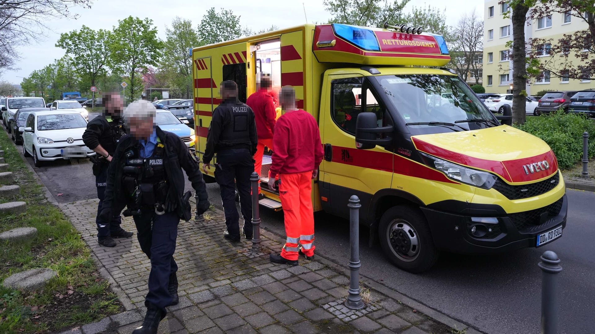 Polizeibeamte und Rettungskräfte stehen vor dem Rettungswagen: Das Opfer der Messerattacke in Dresden-Prohlis wehrte sich gegen die medizinische Hilfe.