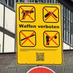 Symbolbild: Ein gelbes Schild mit Piktogrammen und der Aufschrift "Waffen verboten", vor einem Hauptbahnhof. (Quelle: dpa/sulupress)