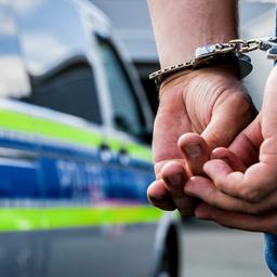 Archivbild: Person steht in Handschellen gefesselt neben einem Polizeifahrzeug. (Quelle: dpa/Schmitt)