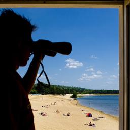 Der Rettungsschwimmer Christian Budschigk von der Deutschen Lebensrettungsgesellschaft (DLRG) beobachtet mit einem Fernglas von einem Turm am Helenesee unweit von Frankfurt (Oder) in Brandenburg die Badenden. (Quelle: dpa/Patrick Pleul)