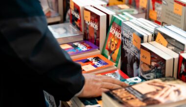 Auf der russischsprachigen Buchmesse in Berlin werden verschiedene russischsprachige Bücher zum Verkauf angeboten. Abgebildet ist ein Tisch, auf dem verschiedene Bücher aufgestellt und gestapelt liegen. Die Hand eines Mannes berührt eines der Bücher.
