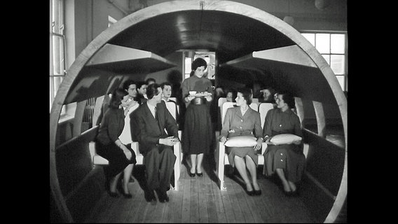 Eine Stewardess in der Ausbildung übt in einem Flugzeug-Nachbau ihre künftige Tätigkeit. © Screenshot 