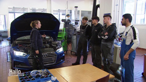Kfz-Mechatronikerin Tabea Opitz erklärt ihren Auszubildenden etwas an einem Auto. © Screenshot 