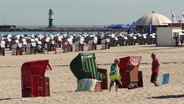 Zwei Personen stehen neben Strandkörben an einem Strand. © Screenshot 