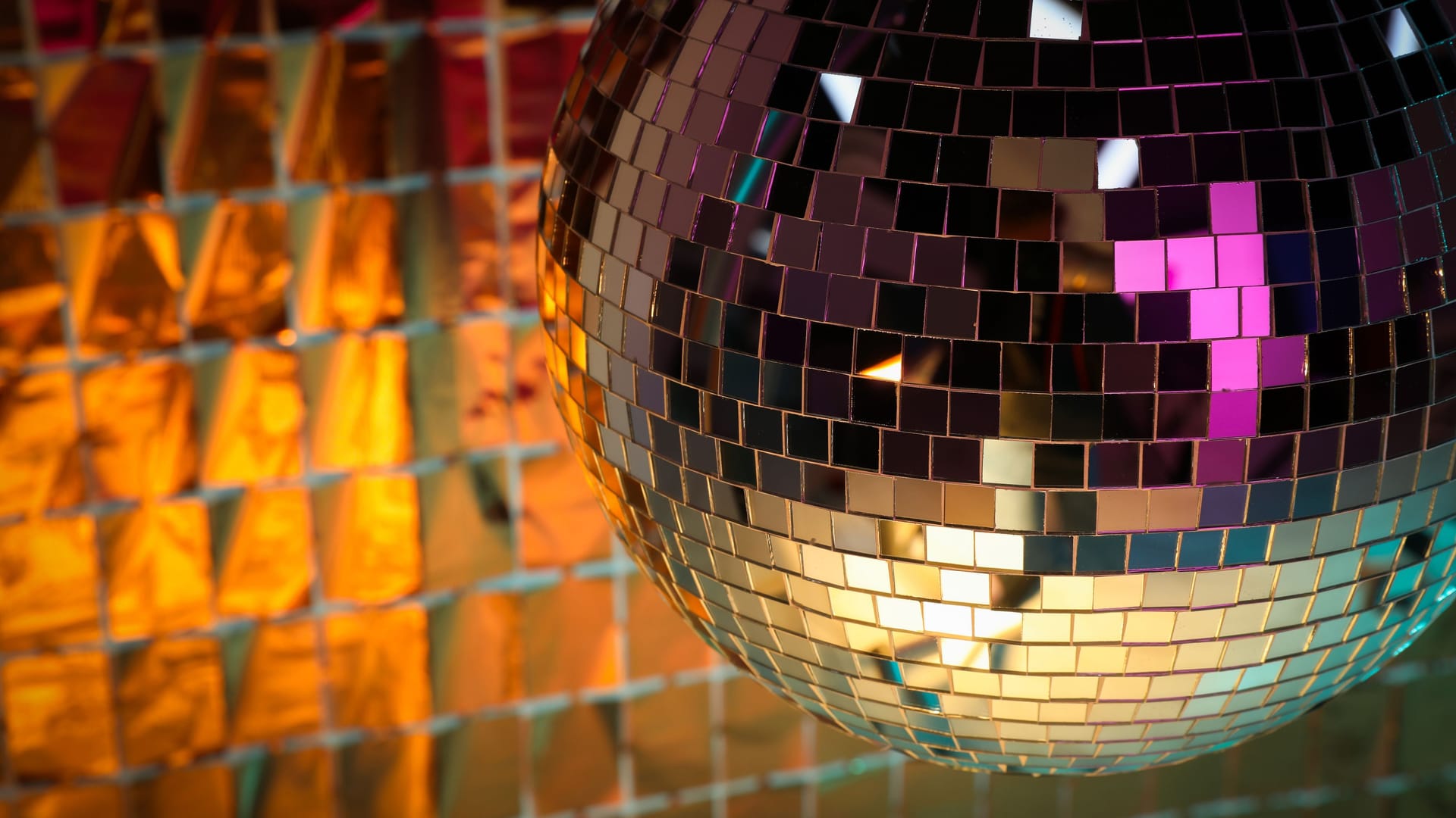 Shiny disco ball against foil party curtain under orange light. Space for text