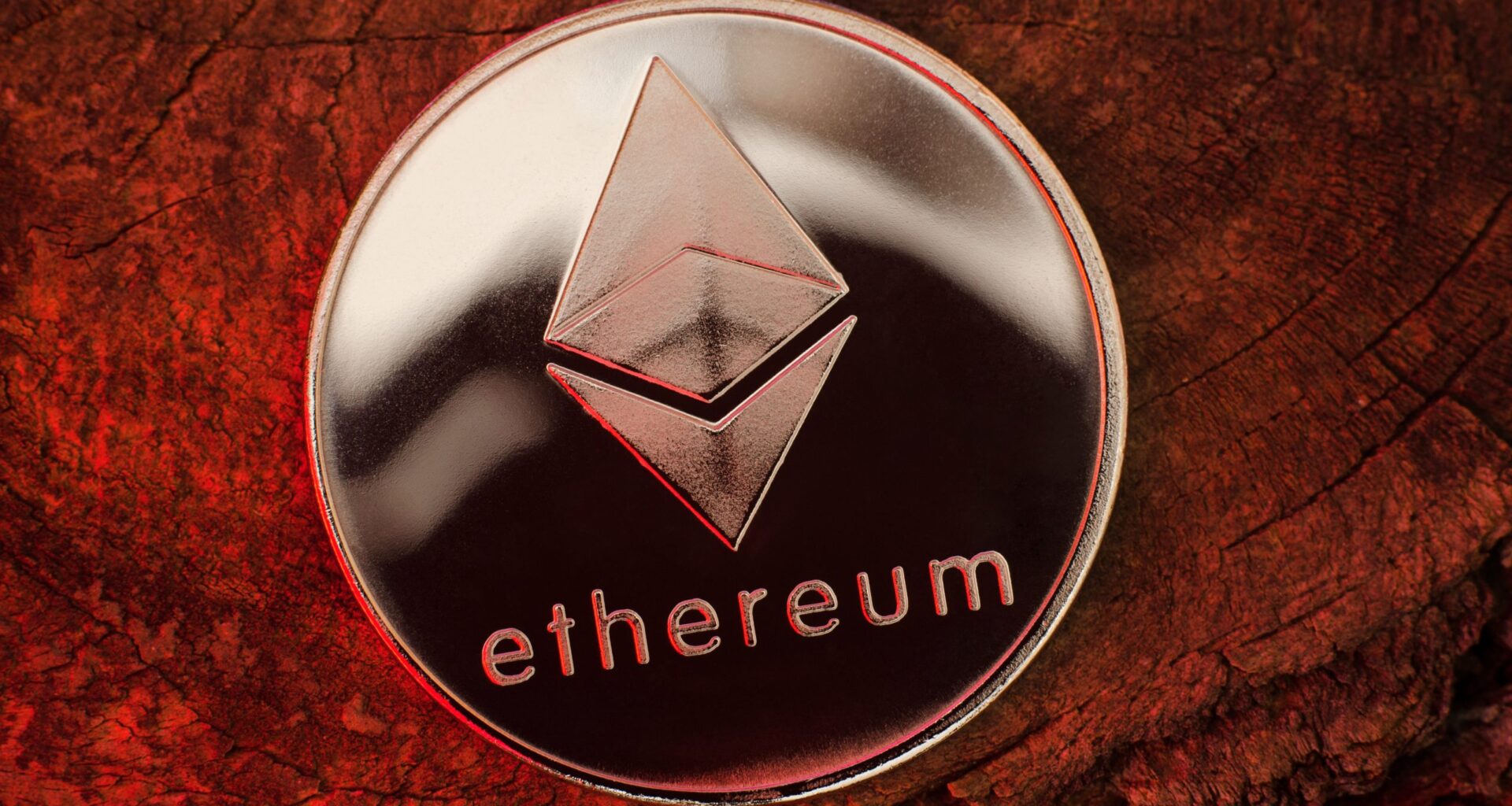 Eine glänzende silberne Ethereum-Münze, die stolz ihr unverwechselbares Logo präsentiert, ruht elegant auf einer strukturierten Holzoberfläche unter einem eindrucksvollen roten Schein.