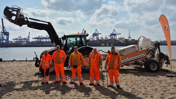 Mitarbeiter der Stadtreinigung stehen vor einem Strand-Traktor mit angehängtem Beachcleaner © NDR/Karsten Sekund 