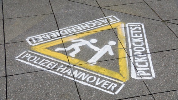 Auf eine Straße in Hannover ist ein Bild gesprüht, welches Passanten vor Taschendiebstahl warnt. © NDR 