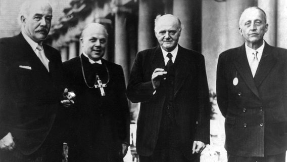 Hinrich Kopf (niedersächsischer Ministerpräsident), Hans Lilje (Landesbischof von Hannover), Rudolf Alexander Schröder (Dichter) und Reinold von Thadden-Trieglaff (von links nach rechts) bei der Eröffnung der deutschen evangelischen Woche am 28. Juli 1949 vor der Stadthalle in Hannover. © picture-alliance Foto: dpa