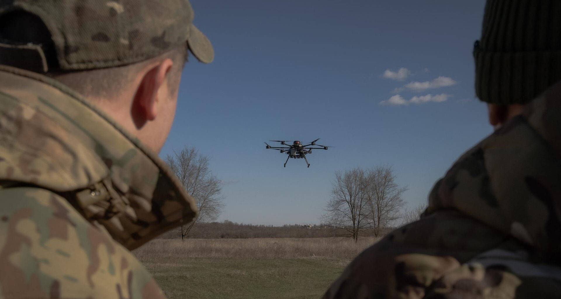 Zwei Militärangehörige beobachten eine Drohne, die über einem Feld aufsteigt.