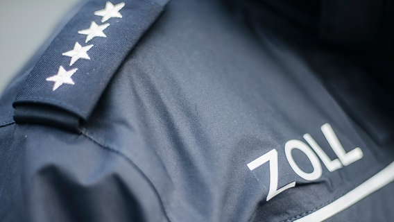 Über der Brusttasche einer blauen Uniform steht das Wort Zoll. © NDR Foto: Julius Matuschik
