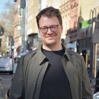Maxi Gstettenbauer steht in der Sonne auf der Ehrenstraße in Köln und lächelt in die Kamera.