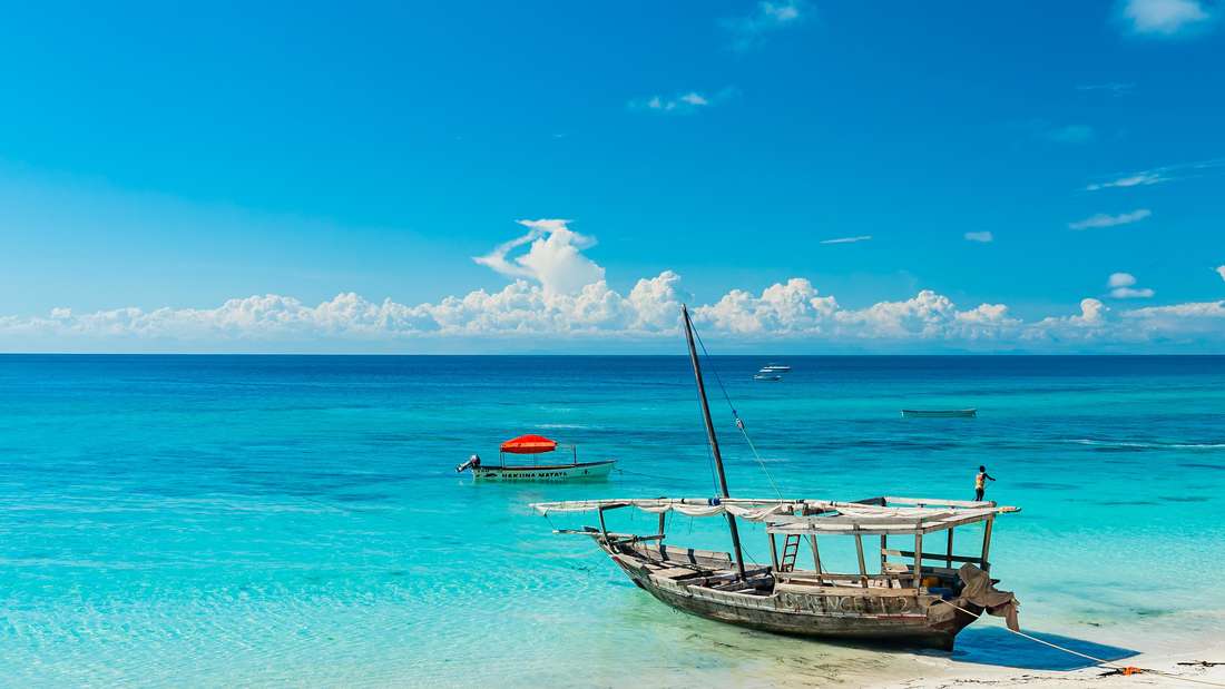 Ein altes Fischerboot liegt am Strand der Insel Mnemba auf Sansibar. Dahinter das blaue Meer. 