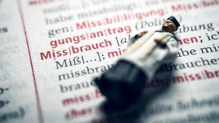 Miniaturfigur eines Priesters in einem Wörterbuch mit dem Wort Missbrauch. Symbolfoto. Zwei Jahre nach Beginn der Untersuchung gibt die Uni Mannheim erstmals Einblick in ihre Studie zu Missbrauchsfällen im Bistum Speyer.