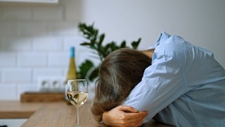 Frau liegt mit dem Kopf auf einem Tisch, vor ihr ein Weinglas. Die Suchtberatungsstelle der Diakonie in Kaiserslautern wird 60 Jahre alt.