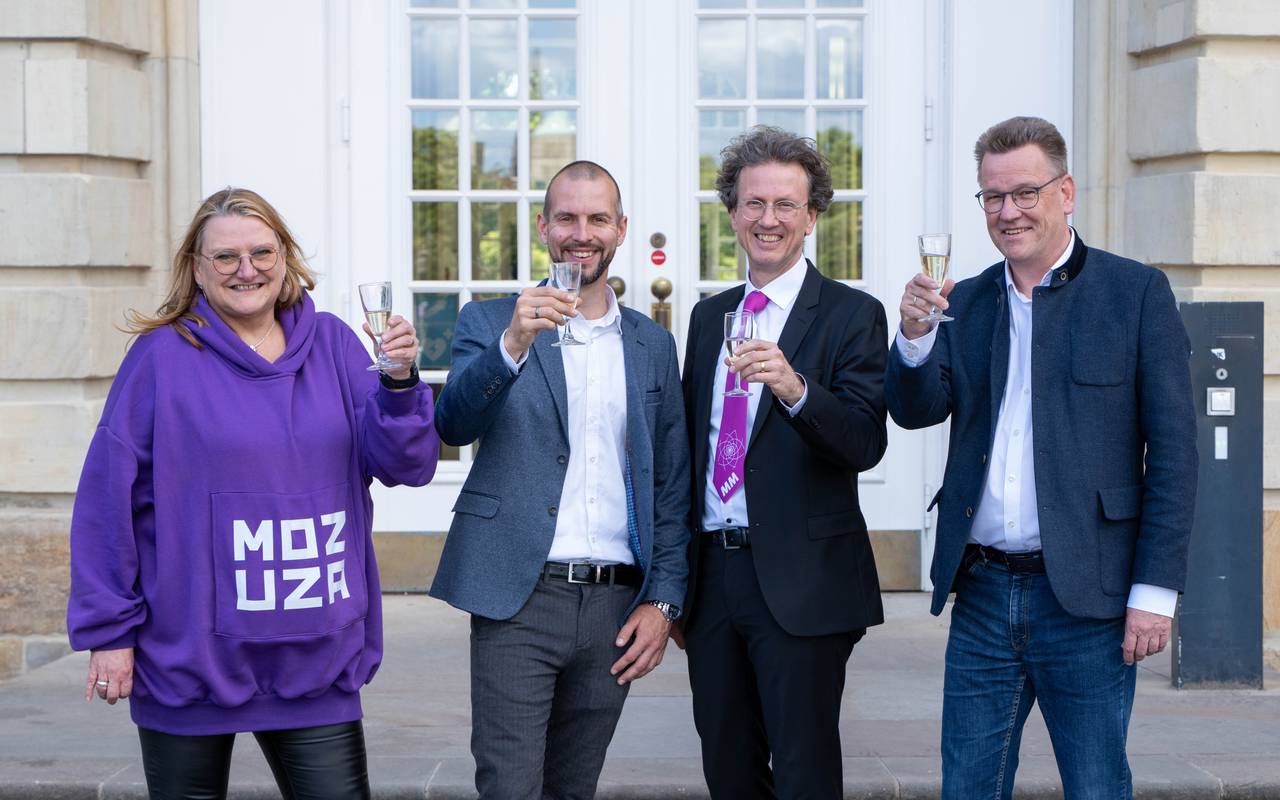 Drei Männer und eine Frau stoßen mit Sekt an.