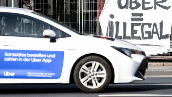 Archivbild: Ein Auto des Mietwagen-Anbieters Uber fährt in Berlin Mitte an einem Plakat mit der Aufschrift «Uber = Illegal» vorbei. (Quelle: dpa/Hofmann)