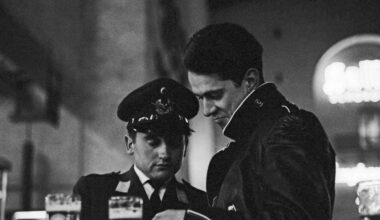 Ein junger Bundeswehrsoldat der Luftwaffe und ein ziviler Begleiter stehen in einer nächtlichen Bahnhofsgaststätte in Westdeutschland. Sie betrachten gemeinsam einen Ausweis oder ein Dokument. Auf dem Tisch davor stehen zwei Gläser Bier. Aufnahme aus den frühen 1960er-Jahren.