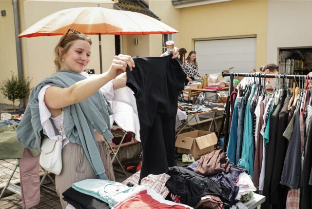Eine junge Frau stöbert Kleidungsstücke auf einem Flohmarkt durch.