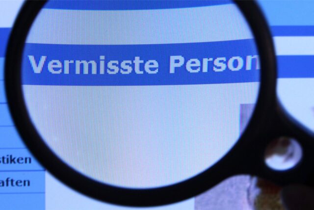 Auf einem Computer-Bildschirm steht „Vermisste Person“, das mithilfe einer Lupe vergrößert wird. (Symbolbild)