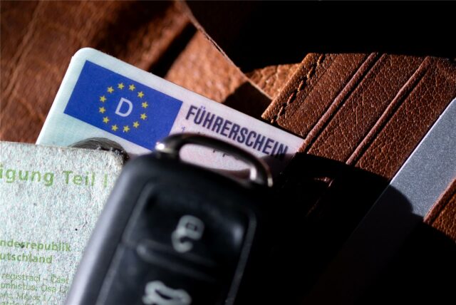 Ein Führerschein, ein Autoschlüssel und eine Zulassungsbescheinigung liegen auf einem Portemonnaie.