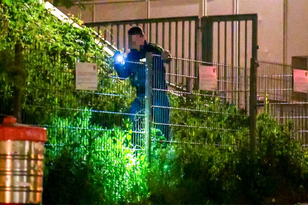 Ein Ermittler der Polizei Dortmund mit einer Taschenlampe hinter einem Zaun