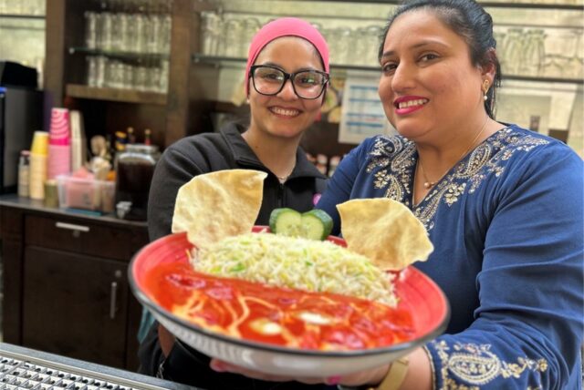 Chefin Navnit Kaur und ihre Nichte Tarandeep Kaur halten im Restaurant Flamingo am Zoo Dortmund einen Teller mit einem indischen Gericht in die Kamera.