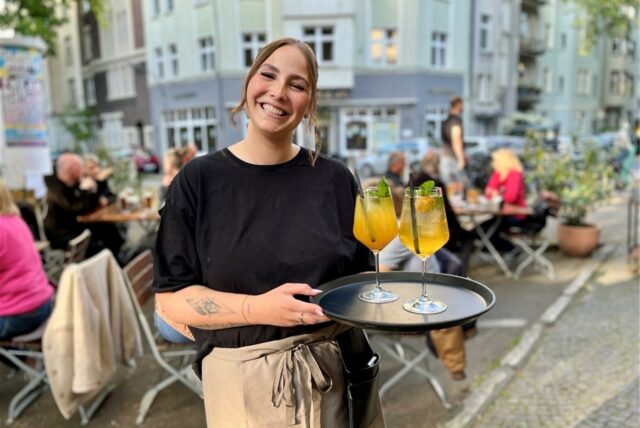 Eine Kellnerin steht mit zwei Getränken vor dem Außenbereich im „Schönes Leben“ im Kreuzviertel.