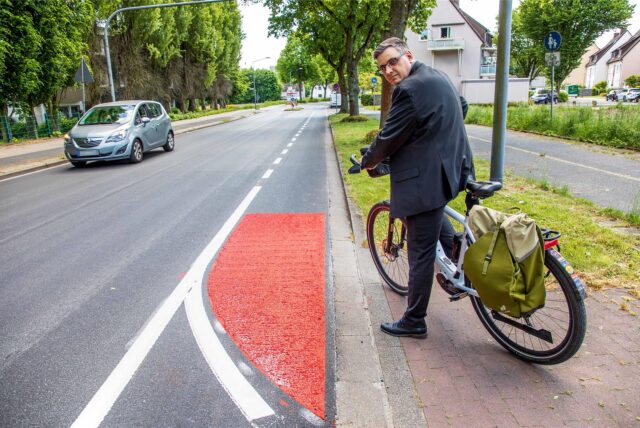 Patrick Berner vom ADFC Vest Recklinghausen steht mit dem Fahrrad an der Straße Über den Knöchel in Herten und blickt über die Schulter.