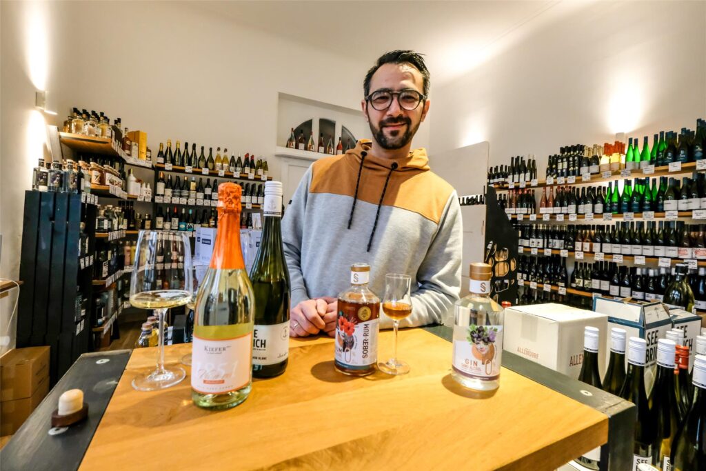 Sebastian Banhold steht in seiner Hertener Weinhandlung hinter einem Tisch, auf dem verschiedene Spirituosen sind.