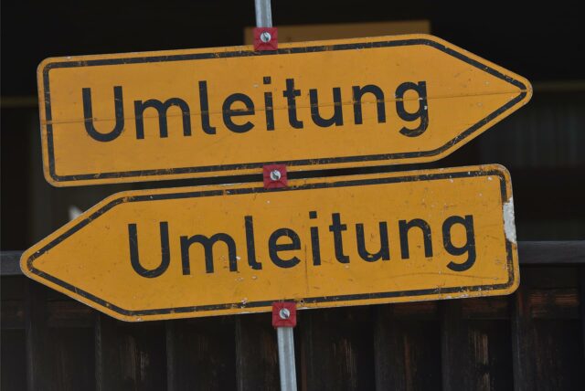 Zwei Umleitungsschilder vor schwarzem Hintergrund.