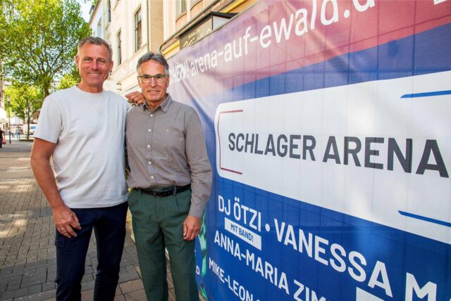 Der ehemalige DFB-Generalsekretär Helmut Sandrock und Ex-Fußball-Profi Ingo Anderbrügge stehen neben einem Plakat der Arena auf Ewald in Herten.