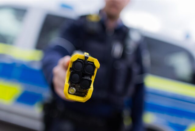 Ein Polizist hält einen Taser (Distanzelektroimpulsgerät) in den Händen.