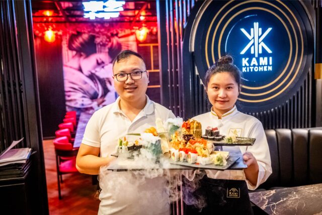 Chef Tri Dung Nguyen und eine Mitarbeiterin halten Sushi-Platten im Restaurant Kami Kitchen am Dortmunder Ostenhellweg in die Kamera