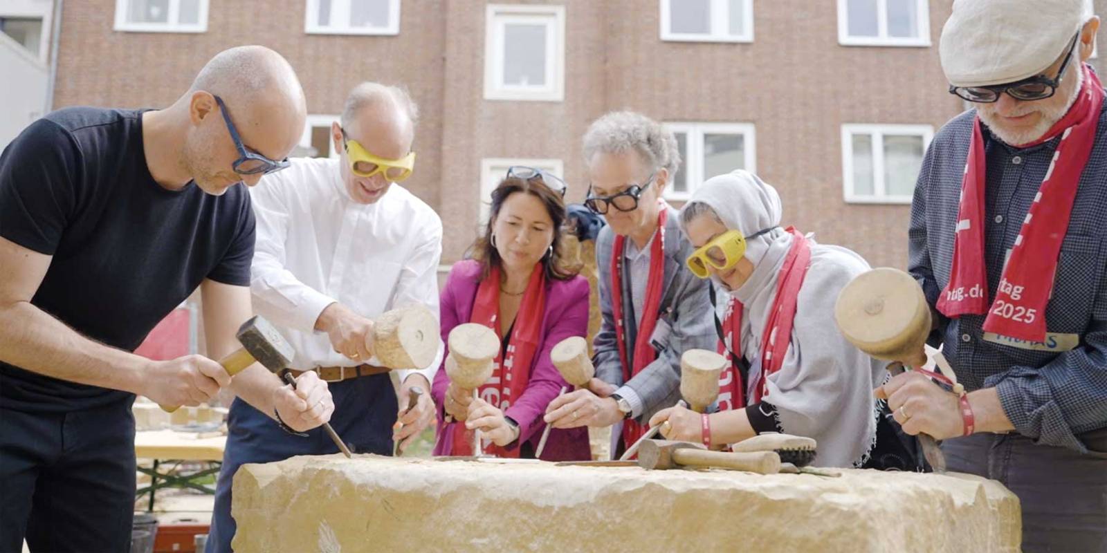 Menschen bearbeiten einen großen Steinblock mit Steinmetzwerkzeugen.