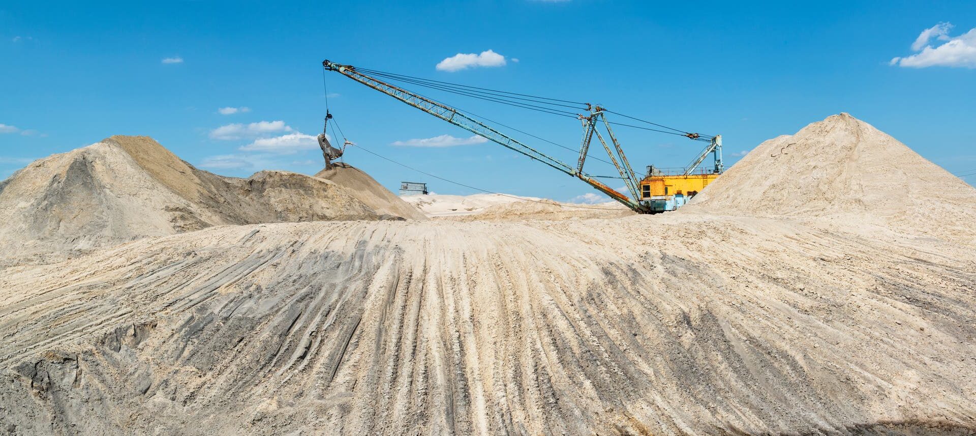 Ein großer industrielle Bagger-Maschine Sand auf einem Hügel in einem Tagebau. Im Vordergrund befindet sich rötliches Wasserteich.